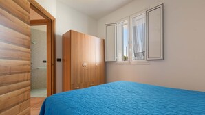 Une chambre à coucher avec une couette matelassée bleue, une armoire en bois et une fenêtre avec des rideaux.