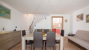 Un coin repas comprenant une table en bois, deux chaises, un canapé et un escalier menant à un niveau supérieur.
