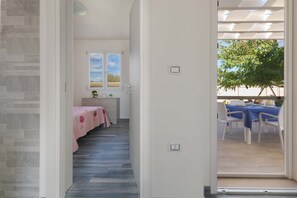 Un couloir menant à une chambre à coucher avec une couvre-lit rose et une fenêtre donnant sur le ciel.