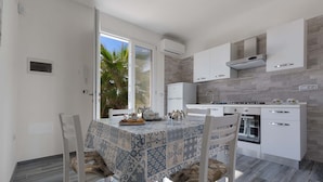 A modern kitchen with white cabinetry, a built-in oven, and a dining area with a patterned tablecloth. - 2092 Villa Il Fenicottero Salentino (Manduria)
