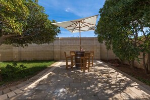 Une terrasse extérieure avec une table et des chaises, un grand parasol et un mur en briques.