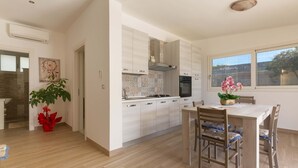 A modern kitchen with white cabinets, a central island, and a dining area with wooden chairs. - 2092 Villa Il Fenicottero Salentino (Manduria)