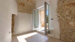 A room with a stone wall, a tiled floor, and a door leading outside. - 2095 Palazzo Benedetto Campo (Torricella)