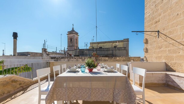 A rooftop terrace with a table set for dining, overlooking a historic town with a bell tower. - 2095 Palazzo Benedetto Campo (Torricella)