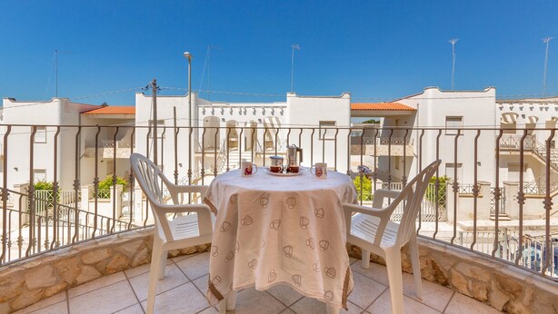 A balcony with a table and chairs, a clear blue sky, and buildings in the background. - 1930 Residence La Primula (Manduria)