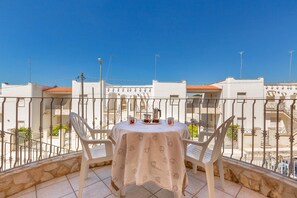 A balcony with a table and chairs, a clear blue sky, and buildings in the background. - 1930 Residence La Primula (Manduria)