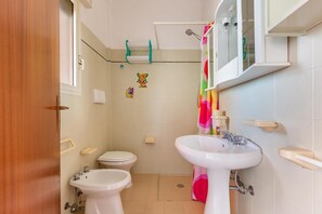 A bathroom with a toilet, bidet, and sink, a shower curtain, and a mirror above the sink. - 1930 Residence La Primula (Manduria)
