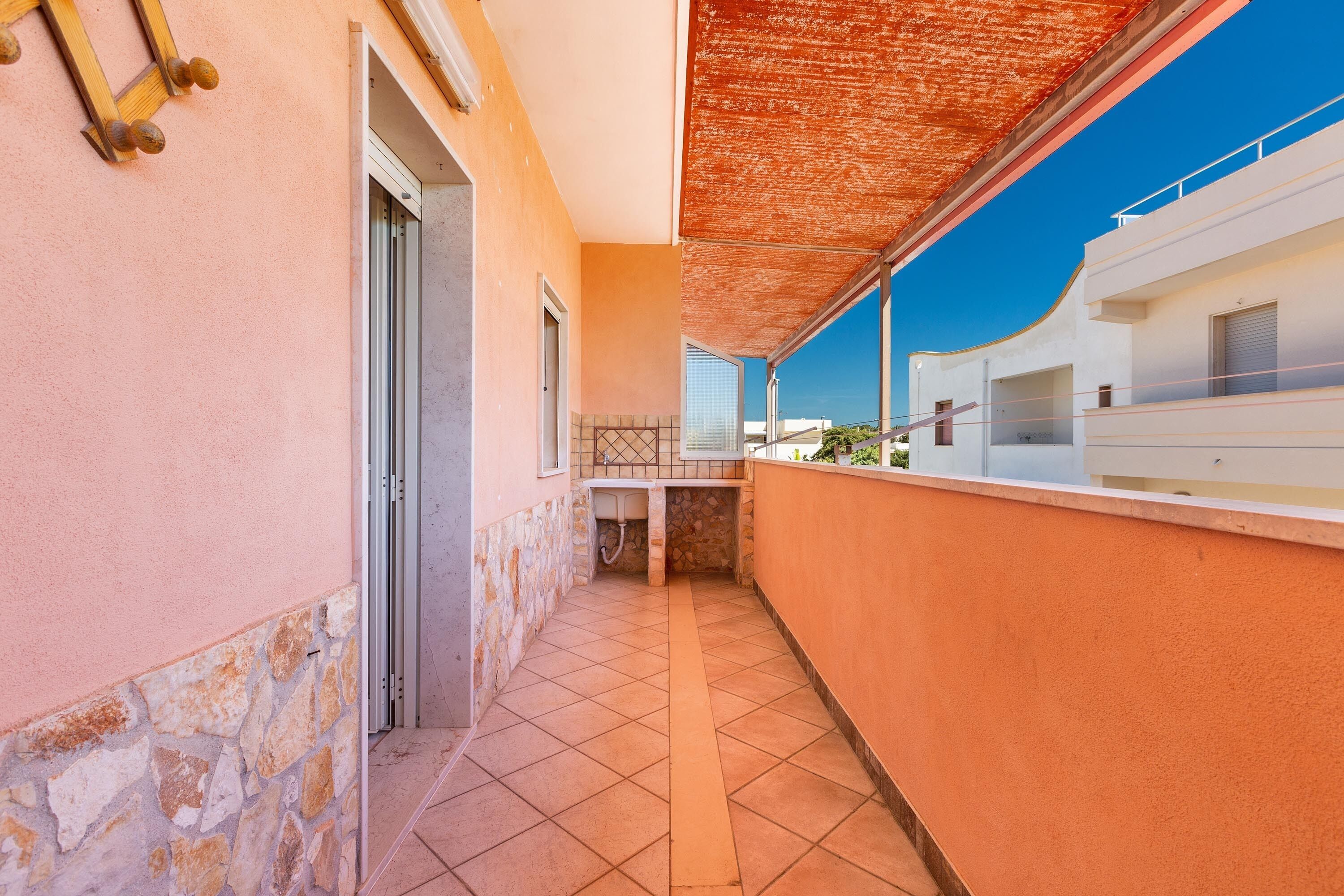 A narrow corridor with a tiled floor, a stone wall on one side, and a balcony with a view of the sky.