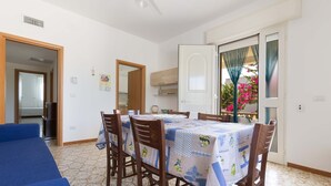 A dining area with a table covered in a blue and white tablecloth, surrounded by wooden chairs. A blue sofa is visible in the foreground. - 2089 Casa Bouganville (Manduria)