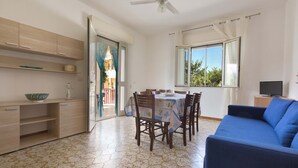 A room with a dining table, chairs, a blue sofa, a TV, and a ceiling fan. - 2089 Casa Bouganville (Manduria)