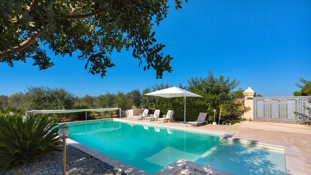 A swimming pool with clear blue water, surrounded by a stone patio and a white umbrella. - 2097 Villa Regina Dello Ionio (Manduria)