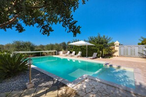 A swimming pool with clear blue water, surrounded by a stone patio and a white umbrella.