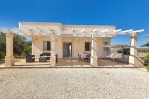 A covered outdoor seating area with a pergola, a table with chairs, and a sofa.