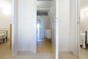 A hallway leading to a bathroom with a shower, a toilet, and a sink.
