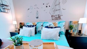 A bedroom with a bed, pillows, a bedside table, a lamp, a wall decoration, and a small plant. - Cozy Seaside Retreat in Rijeka (Rijeka)