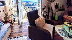 A modern living room with a large window offering a city view, a comfortable seating area, and a decorative plant. - Cozy Seaside Retreat in Rijeka (Rijeka)