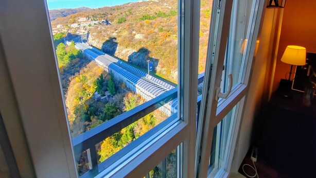A room with a large window overlooking a scenic landscape, including a bridge and distant buildings. - Cozy Seaside Retreat in Rijeka (Rijeka)