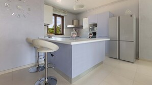 A modern kitchen with a central island, stainless steel appliances, and a decorative clock on the wall. - 2088 Villa Marilda (Martina Franca)