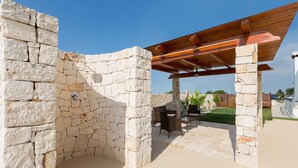 A stone structure with a wooden pergola, outdoor seating, and a clear sky. - 2088 Villa Marilda (Martina Franca)
