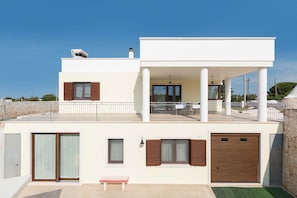 A modern two-story building with a balcony, large windows, and a garage.