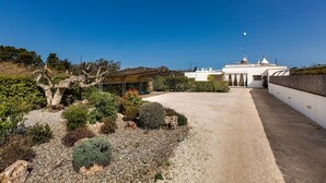 A building with a gravel driveway leading to a covered entrance, surrounded by landscaped gardens and a clear blue sky. - 2124 I Colmi Trulli Suites (Martina Franca)