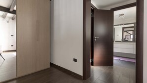 A modern hallway with a wooden door, a light switch, and a mirror reflecting a staircase. - 2094 La Dolce Vita Suite (Avetrana)
