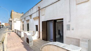 A narrow street with a white building featuring a closed shutter, a metal railing, and a tiled sidewalk. - 2094 La Dolce Vita Suite (Avetrana)
