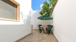 A small patio area with a table and chairs, a green-striped umbrella, and a window. - 2094 La Dolce Vita Suite (Avetrana)