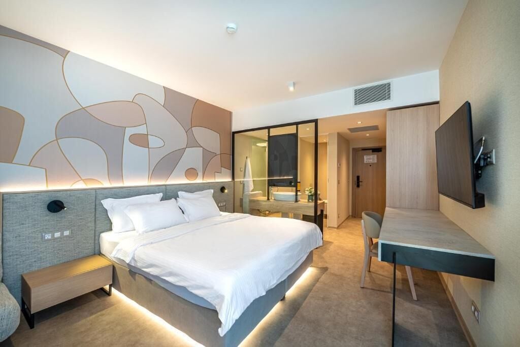 Una habitación de hotel moderna con una cama, mesita de noche, escritorio y un espejo grande.