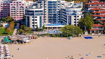 Ein Strandhotel mit mehreren Gebäuden, einem Sandstrand und klarem, blauem Wasser.