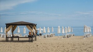 Una playa con un pabellón, sillas reclinables blancas y sombrillas.