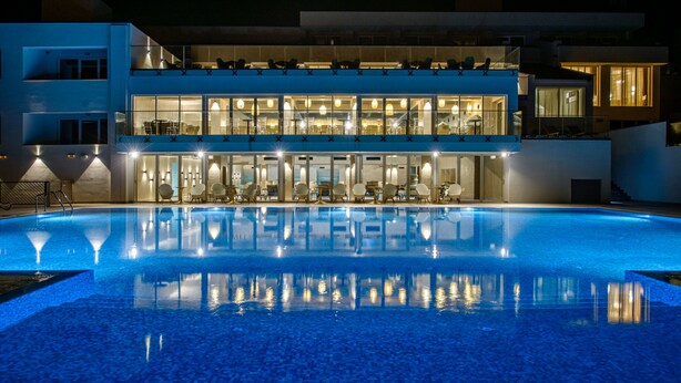 Ein modernes Hotel mit großem Schwimmbad, mehreren Balkonen und einem gut beleuchteten Innenbereich.