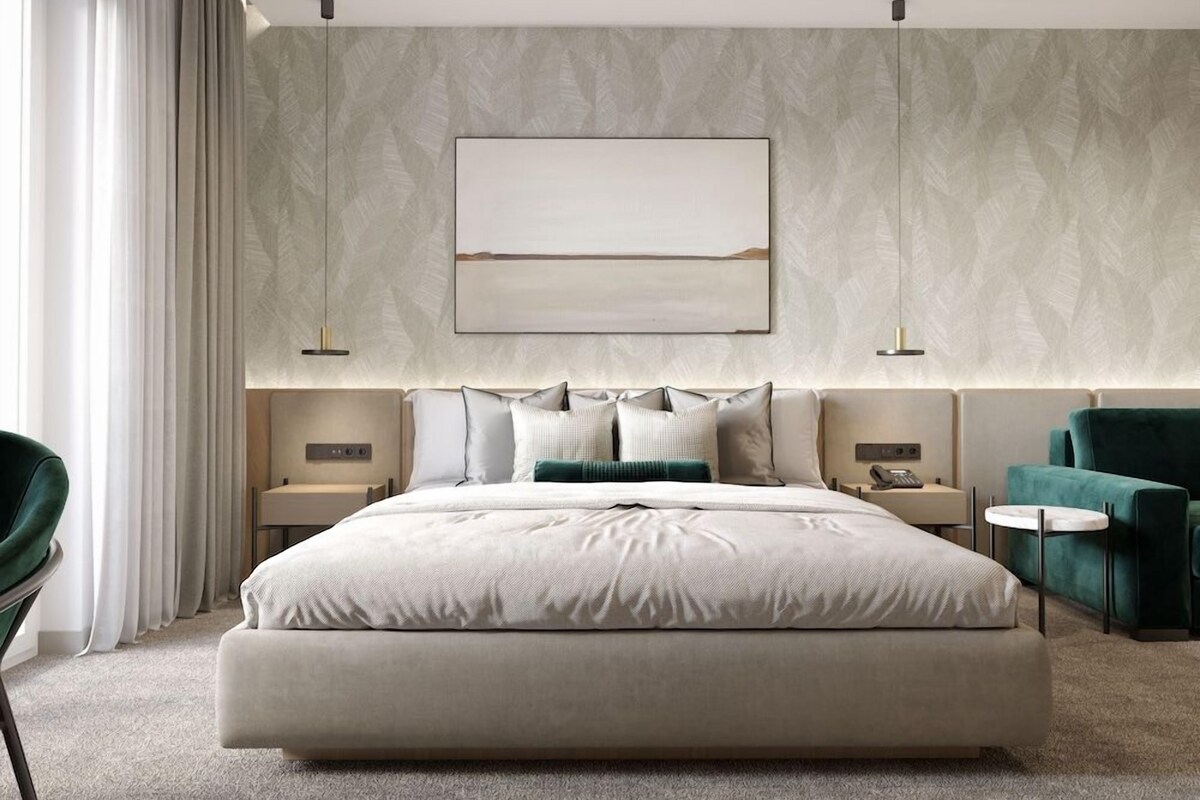 A modern hotel room with a large bed, two bedside tables, a green armchair, and a large abstract painting on the wall.