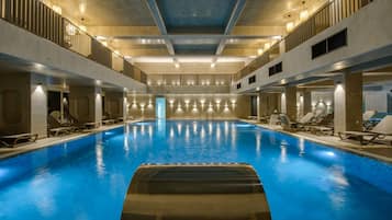 A large indoor swimming pool with multiple lanes, surrounded by lounge chairs and a high ceiling with exposed beams.