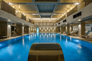 A large indoor swimming pool with multiple lanes, surrounded by lounge chairs and a high ceiling with exposed beams.