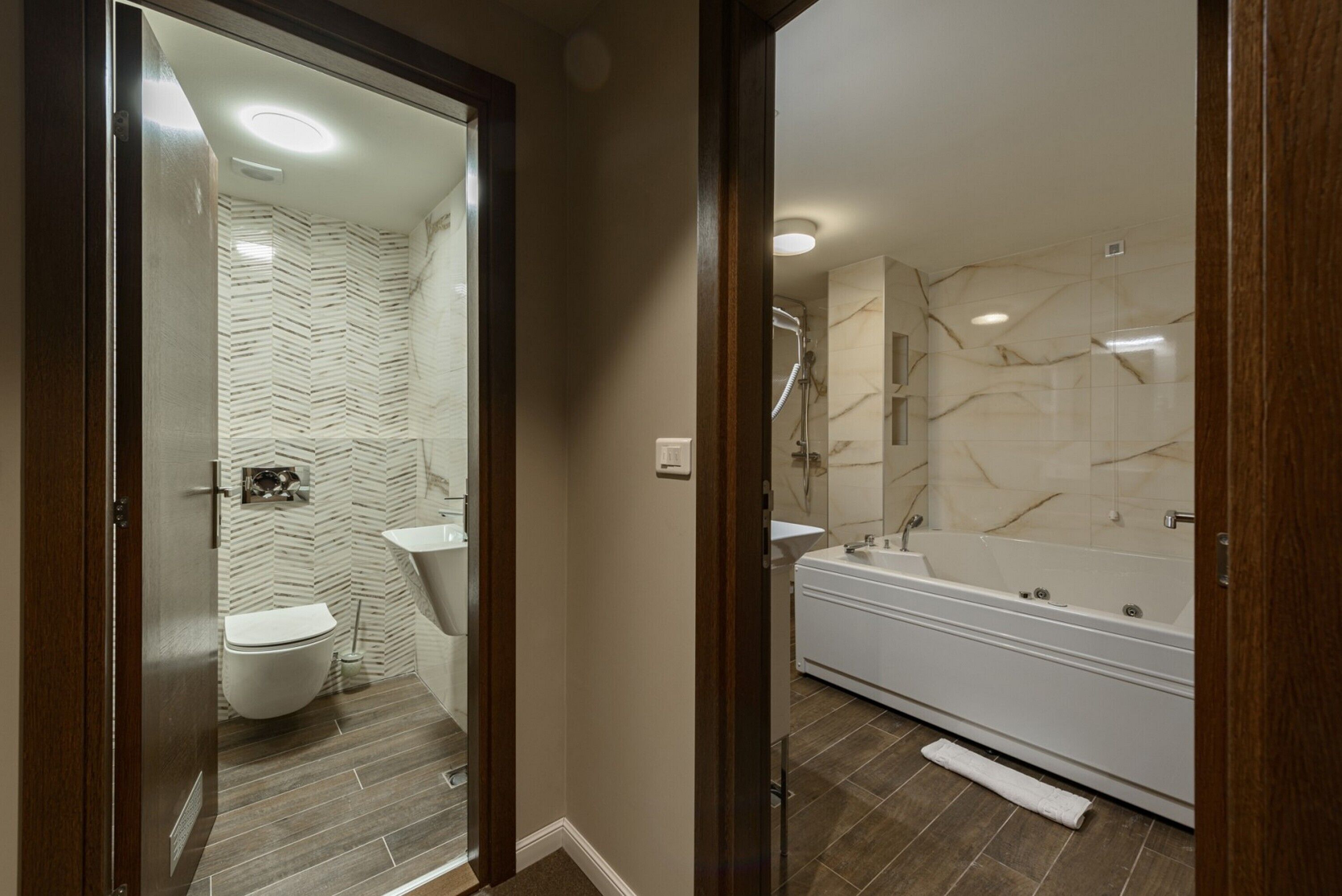 A modern bathroom with a herringbone-patterned wall, a white toilet, a sink, and a large bathtub.
