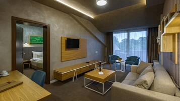 A modern hotel room with a bed, a wooden desk, a sofa, a TV mounted on the wall, and a large window with a view.