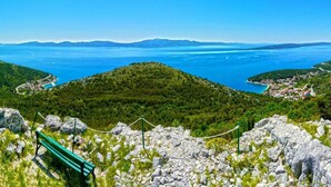 Un paysage montagneux offrant une vue dégagée sur une zone côtière, une route sinueuse et un banc vert.