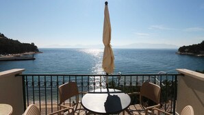 Un balcon avec une table et des chaises donnant sur une étendue d’eau, avec des montagnes visibles au loin.