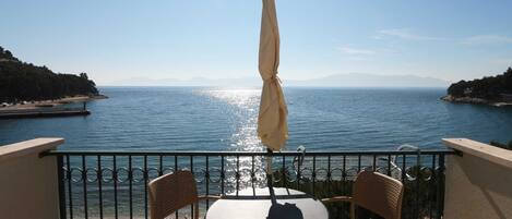 Un balcon avec une table et des chaises donnant sur une étendue d’eau, avec des montagnes visibles au loin.