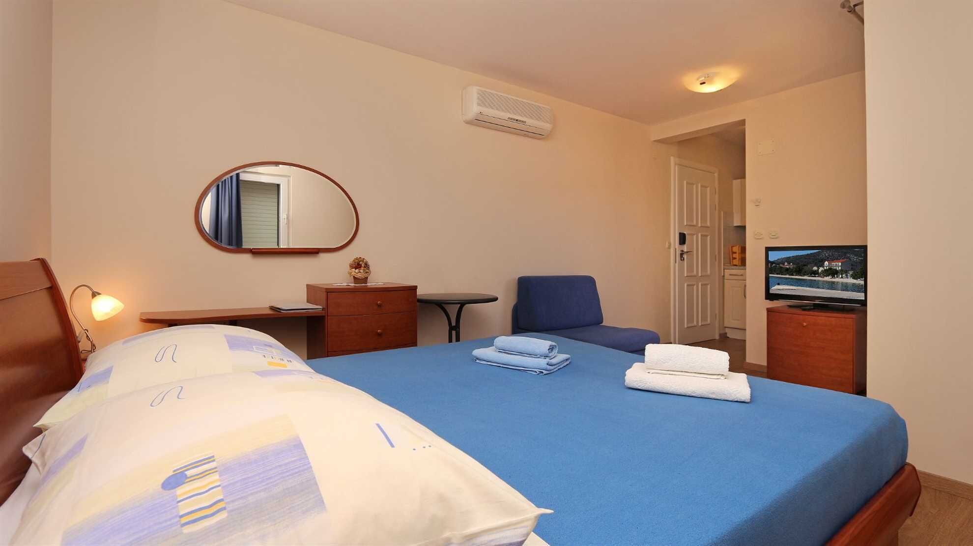 A hotel room with a bed, a desk, a chair, a television, and a mirror.
