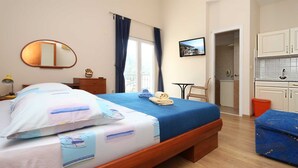 Habitación de hotel con cama, escritorio, silla, una mesita, espejo, un cuadro en la pared y una zona de cocina.