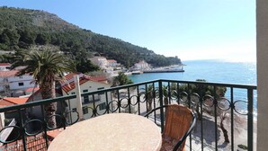 Un balcón con una mesa redonda y sillas, con vista a una zona costera con edificios y una vista despejada del mar.