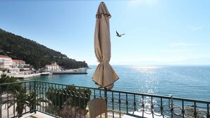 Uma varanda com vista para o mar, uma cadeira e um guarda-sol suspenso.