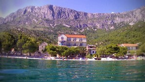 A coastal building with a red roof, surrounded by trees and a mountainous backdrop. - Sea View Apartment 33 (Drvenik)