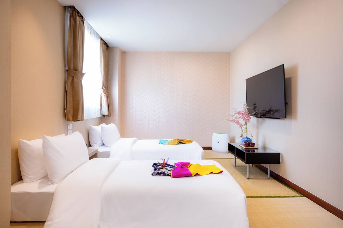 Une chambre d’hôtel avec deux lits, un téléviseur à écran plat, une petite table et un vase avec des fleurs.