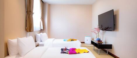 A hotel room with two beds, a flat-screen TV, a small table, and a vase with flowers.