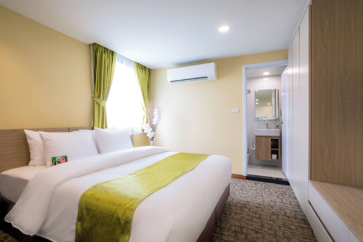 Une chambre d’hôtel avec un grand lit, une salle de bain visible à travers une porte ouverte et un rideau vert.