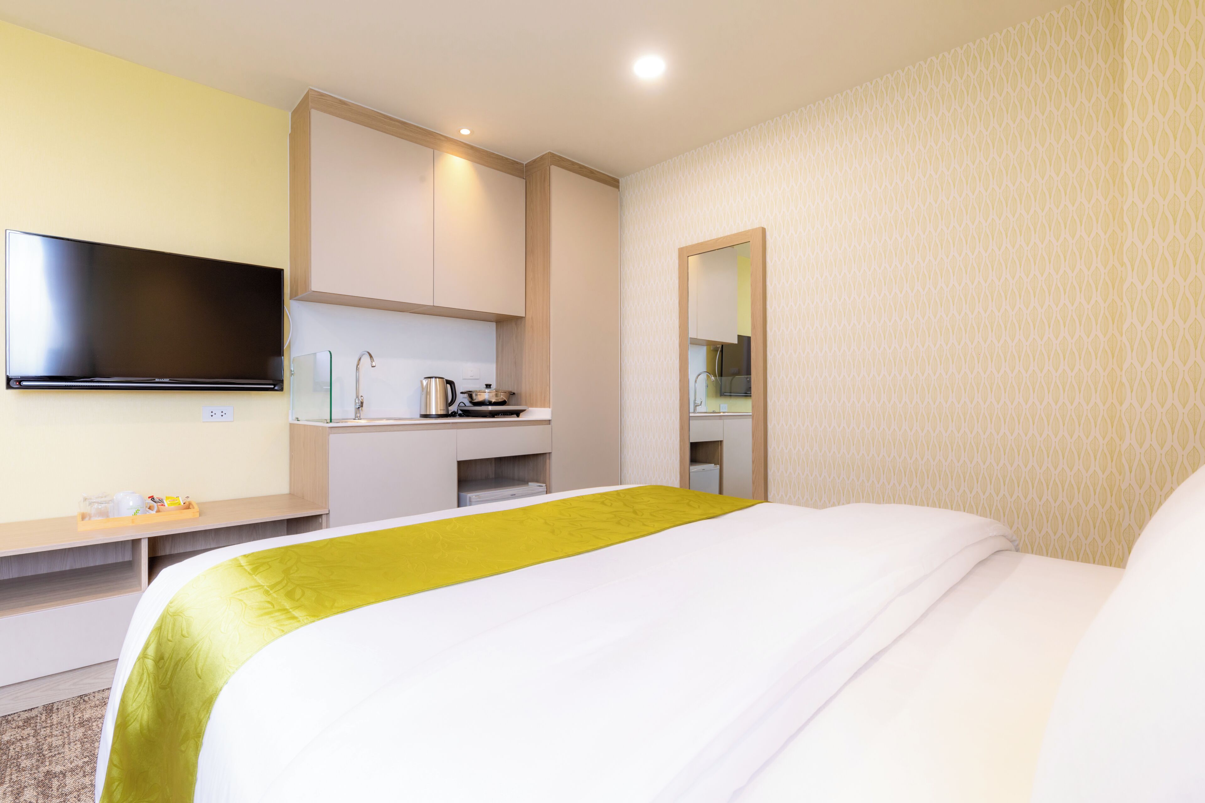 Habitación de hotel con cama, televisor de pantalla plana en la pared, kitchenette pequeña y espejo.