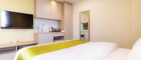 Habitación de hotel con cama, televisor de pantalla plana en la pared, kitchenette pequeña y espejo.